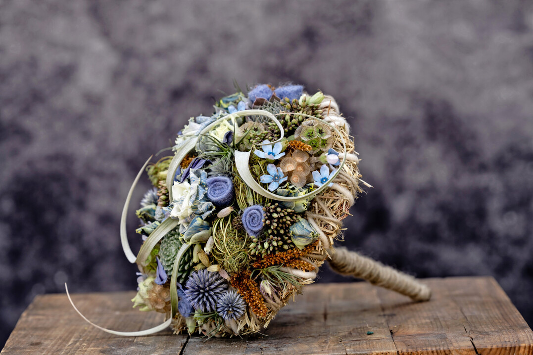 Den blauen Brautstrauß fertigte der ungarische Floristmeister Krisztián Kövér. Er kombinierte zu blauen Blüten und natürlichem Heu die Wollkordel „Dochtfaden“ in gebrochenem Weiß in 5 mm Stärke und die dünnere Wollschnur „Smartfaden“ in Porzellanweiß.