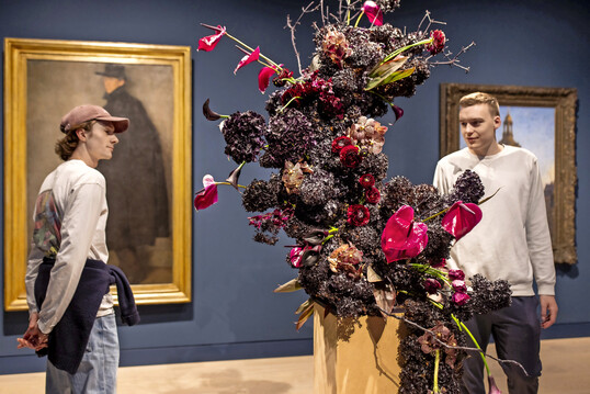 Wilhelm Schmurr: „Bildnis Werner Heuser“, 1902, floral interpretiert von Christina Janet Schacke,
Blumenhaus am Hofgarten
: „Gegen den Strom“ mit
<i>Vanda</i>
,
<i>Calla</i>
,
<i>Scabiosa </i>
und Aubergine