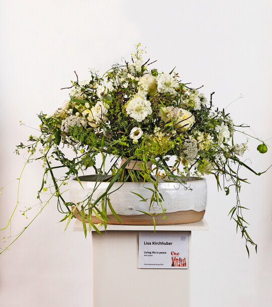 <b>Lisa Kirchhuber</b>
 beschrnkte sich in ihrem Strau Living life in peace auf weie Blumen, wobei Rosen, Knautien und 
<i>Lisianthius </i>
von kleinbltigen Floralien und cremeweien 
<i>Hypericum</i>
-Frchten begleitet werden. Die Blumen sind in sattgrnes Laub eingebettet und werden von hellgrnen Ranken umspielt.