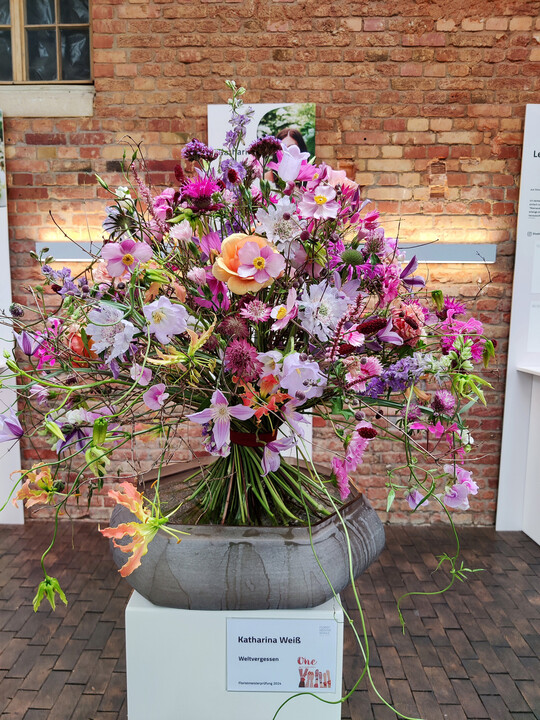 <b>Katharina Wei</b>
 gelang bei der Meisterprfung 2024 der beste Strau. Die Floristmeisterin kombinierte unter dem Namen Weltvergessen Blten in groer Formenvielfalt. Farblich spielen helle sowie satte Rosa- und Violetttne die Hauptrolle, lachsfarbene Rosen und 
<i>Gloriosa</i>
 sorgen fr Kontrast und eine lebendige Ausstrahlung. 