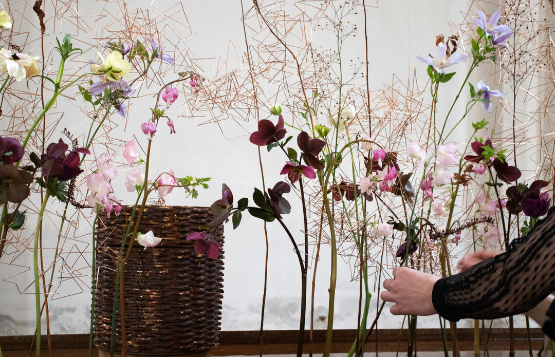 Dem kantigen Draht, der als Steckhilfe fungiert, stehen die Zartheit und Zerbrechlichkeit der floralen Werkstoffauswahl gegenber. Die schwebenden Blumen erinnern an Vgel oder Flgel, sie umschwirren die Urne wie im Aufbruch.