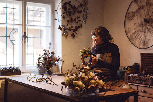 Zwischen alten Mauern und frischem Grün: Lisa Hartleitner arbeitet an einem ihrer charakteristischen, wild gebundenen Kränze. Die Floristin verarbeitet regionales Pflanzenmaterial zu nachhaltigen, lebendig wirkenden Werkstücken.