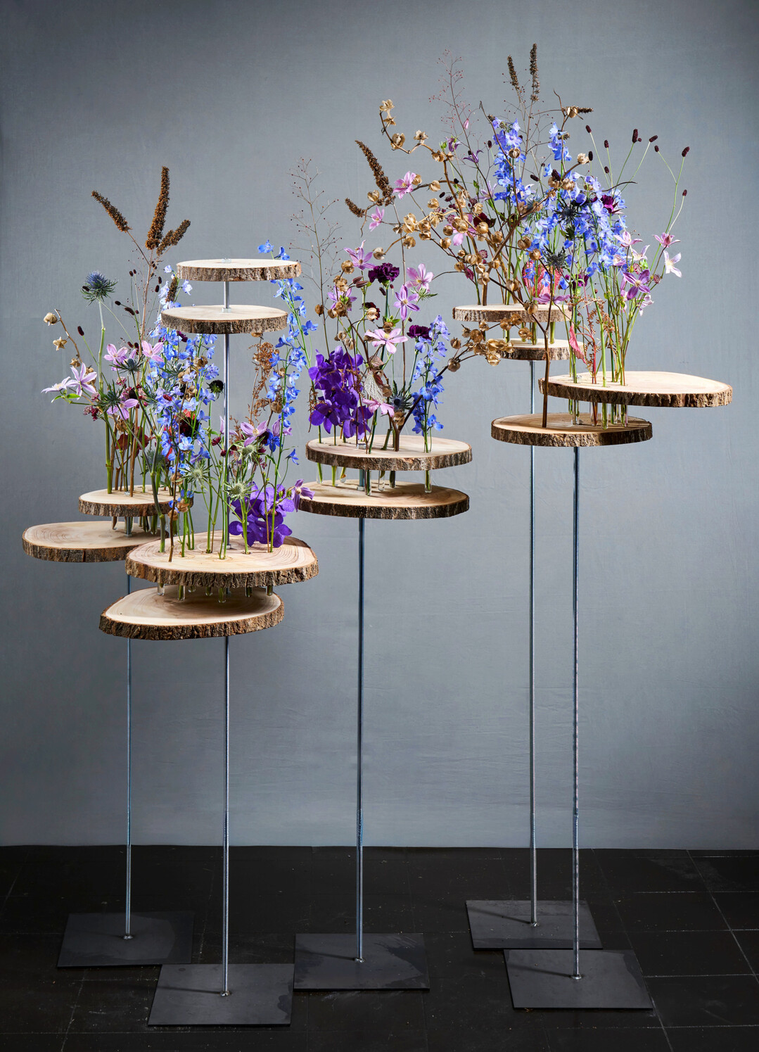 For this layered decorative arrangement on stands, Elisabeth Schoenemann drilled holes in tree discs and mounted them on 16 mm threaded rods. Dry branches provide a sense of movement to the fresh flowers in test tubes. 