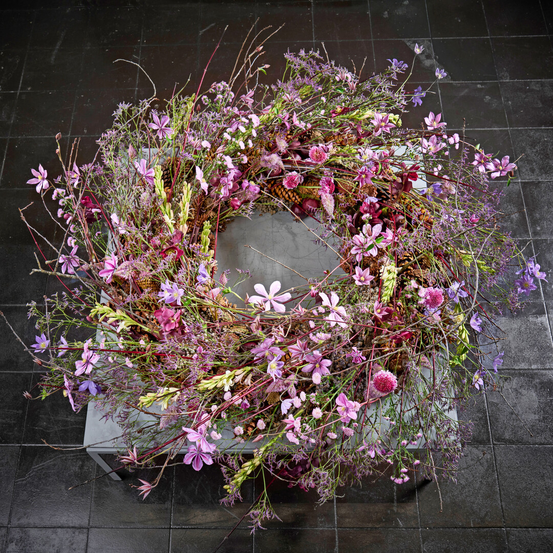 Sara-Lisa Ludvigsson creates a floral explosion of delicate blossoms in shades of lilac. The clematis resemble butterflies, which, together with the other flowers, playfully frame the compactly arranged wreath base made of pine cones. 