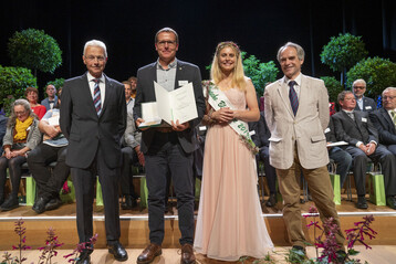 Martin Becker (Mitte) nahm den Staatsehrenpreis in Empfang von Dr. Thomas Schmidt (BMEL/rechts). Es gratulierten Hartmut Weimann (ZVG/links) und Blumenfee Annika Stroers 